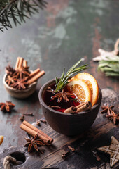 Mulled wine in ceramic mug with orange slices and spices. Christmas hot drink on wooden table with xmas tree branches, festive card text space