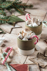 Hot drink with marshmallows and candy cane in green mug. Fir tree decor in the background. Cozy seasonal holidays. Concept of christmas or new year drink