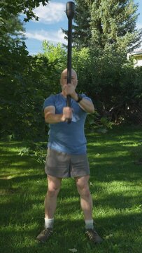 senior, athletic man is exercising with a steel mace performing 360 movement, summer scenery