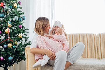 Mother hugging cute daughter in pajamas and laughing. Christmas holidays at home. High quality photo