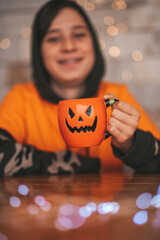 Portrait of candid authentic zoomer boy posing with jack lantern mug and sweets at halloween party