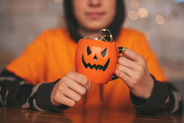 Portrait of candid authentic zoomer boy posing with jack lantern mug and sweets at halloween party