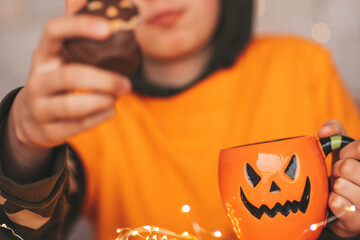 Portrait of candid authentic zoomer boy posing with jack lantern mug and sweets at halloween party