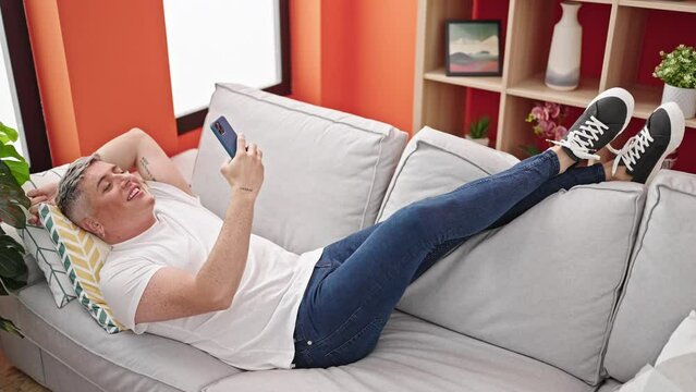 Young caucasian man taking selfie picture with smartphone lying on the sofa at home