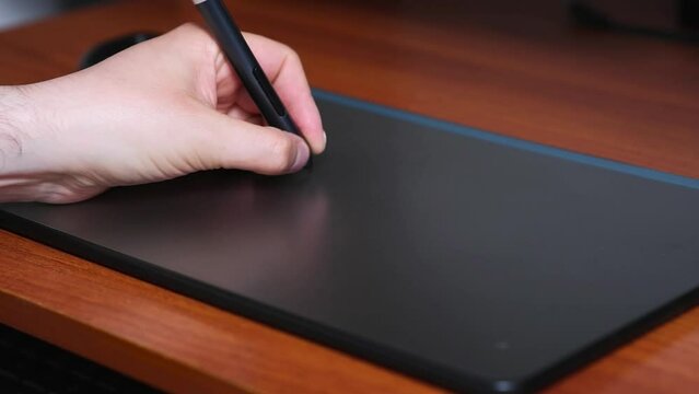 Left hand draws on digital board that is on wooden table, graphic designer work, digital tool