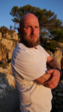Striking portrait of a man with blue eyes and a beard, set against the picturesque landscape of Cap d'Antibes, France. His tattoos tell a story, embodying a blend of rugged charm and natural beauty