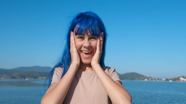 Hopeful blue teen by sea. A view of hopeful blue haired teen girl look with surprise on the beach under sun.