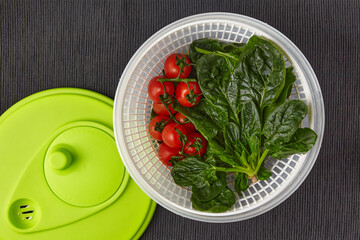 Washed cherry tomatoes and spinach in a spinning colander on a black textile tablecloth. Healthy light food. Top view with copy space