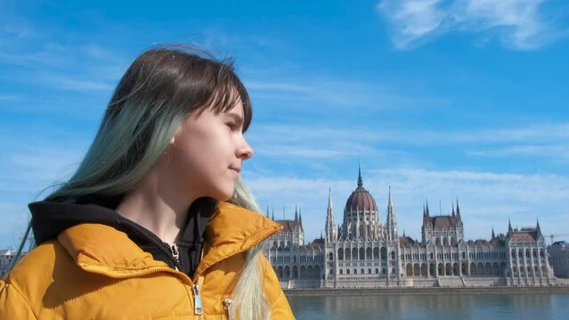Girl near budapest parliament building. A tourist girl stand near the Danube river and admire the Budapest parliament in the sun light.