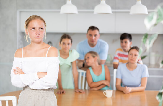 miffed teenager gir with arms crossed over chest standing in front of her big family