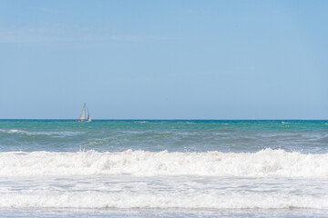 Fototapeta na wymiar Breaking waves on the seashore and a sailboat in the background.