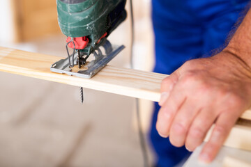 Cropped view of man using a jigsaw machine on wooden plank at home