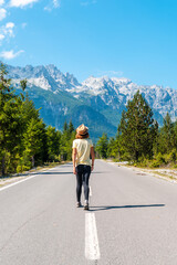 A tourist in summer walking on the road in the Valbona valley next to trees, Theth national park, Albanian Alps, Albania. vertical photo