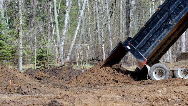 Dump truck with the steel bed up unloads its cargo of dirt at a home building construction site.