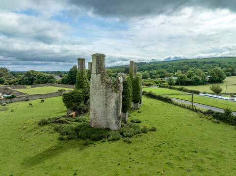 Aerial view of Castlecuffe castle in Ireland, ruined tower house with chunks of corner walls with stone chimneys standing on a green meadow 
