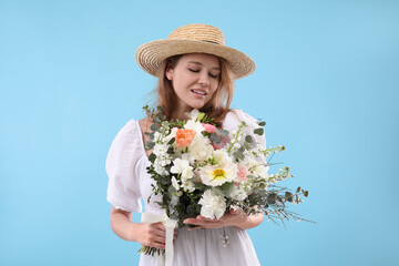 Beautiful woman in straw hat with bouquet of flowers on light blue background