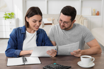 Young couple with papers discussing pension plan at wooden table indoors