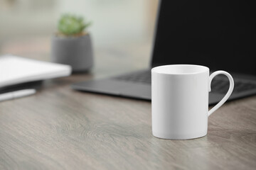 White ceramic mug and laptop on wooden table indoors. Space for text