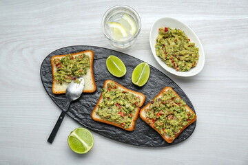 Delicious sandwiches with guacamole and lime wedges on white wooden table, flat lay