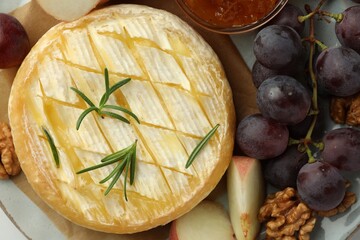 Tasty baked brie cheese with rosemary, fruits and walnuts on plate, top view