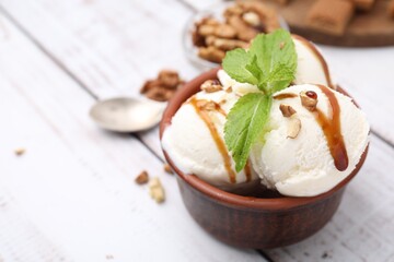 Bowl of tasty ice cream with caramel sauce, mint and nuts on white wooden table, closeup. Space for text