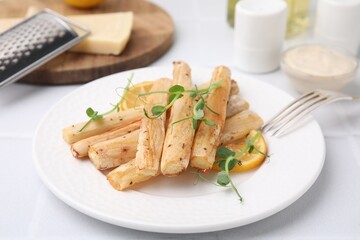 Plate with baked salsify roots and lemon on white table, closeup