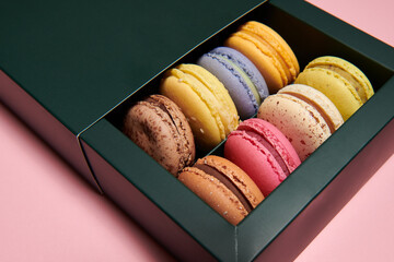 Dark green box with assorted macaroons on the pink background. Colorful desserts with different filling. Closeup.