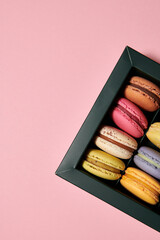 Dark green box with assorted macaroons on the pink background. Colorful desserts with different filling. Free space for text. Vertical photo.