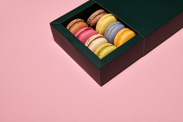 Dark green box with assorted macaroons on the pink background. Colorful desserts with different filling. Free space for text. Horizontal photo.