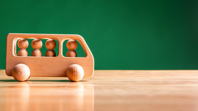 Wooden public bus and passengers model on the table with green background. Transportation and education concept.