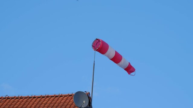Striped White and Red Windsock Wind Cone Wind Sleeve Indicator Installed on Roof of General Aviation Airport Building Showing Wind Speed and Direction To Pilot Operating Airplane