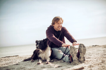 Middle aged man sitting with his dog on the beach