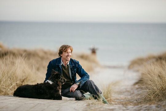 Middle aged man sitting with his dog on the beach