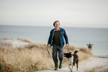 Middle aged man walking his dog on the beach - Powered by Adobe