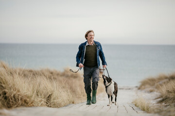 Middle aged man walking his dog on the beach