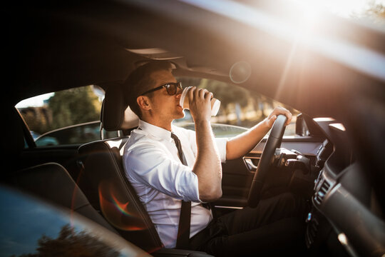 Young caucasian businessman drinking coffee while driving to work
