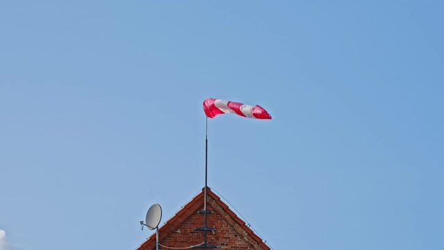 Striped White and Red Windsock Wind Cone Wind Sleeve Indicator Installed on Roof of General Aviation Airport Building Showing Wind Speed and Direction To Pilot Operating Airplane