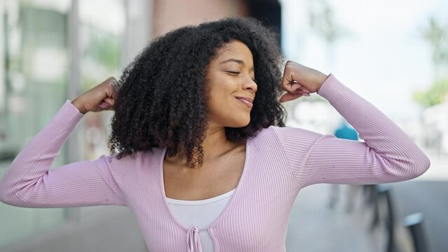 African american woman smiling confident doing strong gesture with arms at street