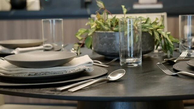 Close up of fancy round black dining table with elegant dinner tableware, napkins and flowerpot in modern kitchen. Concept of hospitality and catering