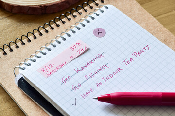crossed out events in a checklist or To-do list. An woman's preference to have indoor tea party instead of outdoor activities due to hot and humid summer day. Selective focus.