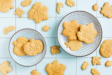 Freshly baked homemade cookies in the form of autumn leaves and Halloween pumpkins in plates with a blue pattern on a tiled background.