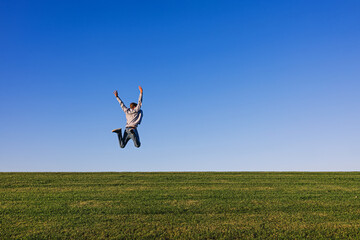 Happy man enjoying fresh air, jumping on the horizon on the green grass