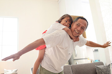 Grandfather carrying his granddaughter on his back, playing like a plane at home