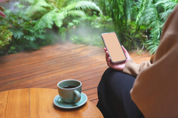 Mockup image of a woman holding mobile phone with blank white desktop screen in the garden