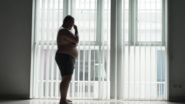 Asian overweight man thinking something while looking out the window
