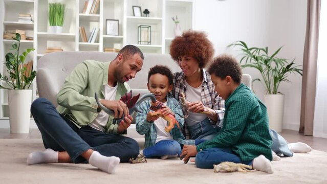 African american family in casual attire playing toys with school-aged sons on floor. Loving father and mother creating happy childhood for children while spending time together in modern apartment