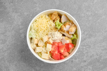 Top view of salad with chicken meat, cheese, tomatoes and crouton in cardboard bowl