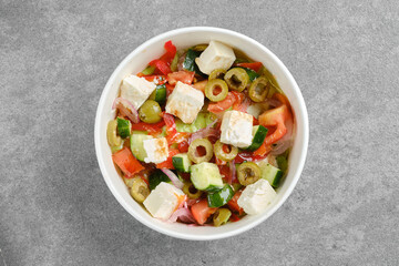 Top view of salad with feta cheese, tomatoes, iceberg lettuce and olives in cardboard bowl