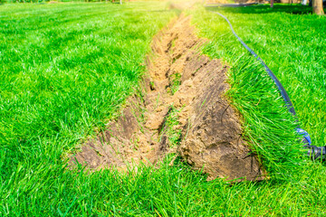 A ditch dug in the lawn for laying pipes and installing irrigation. Soil under green lawn and grass...