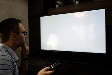 Man watching television, turning on plasma flatscreen TV-set, pointing remote control at empty TV...